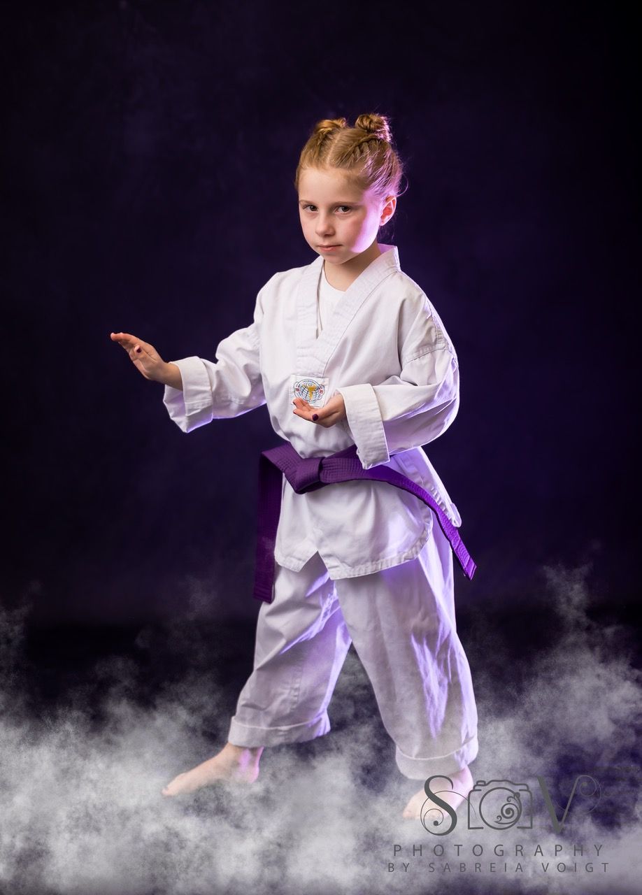 Young person in karate uniform, purple belt, in fighting stance on a smoky dark background.