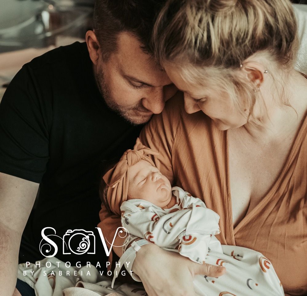 Parents cradling newborn baby; soft light, neutral colors.