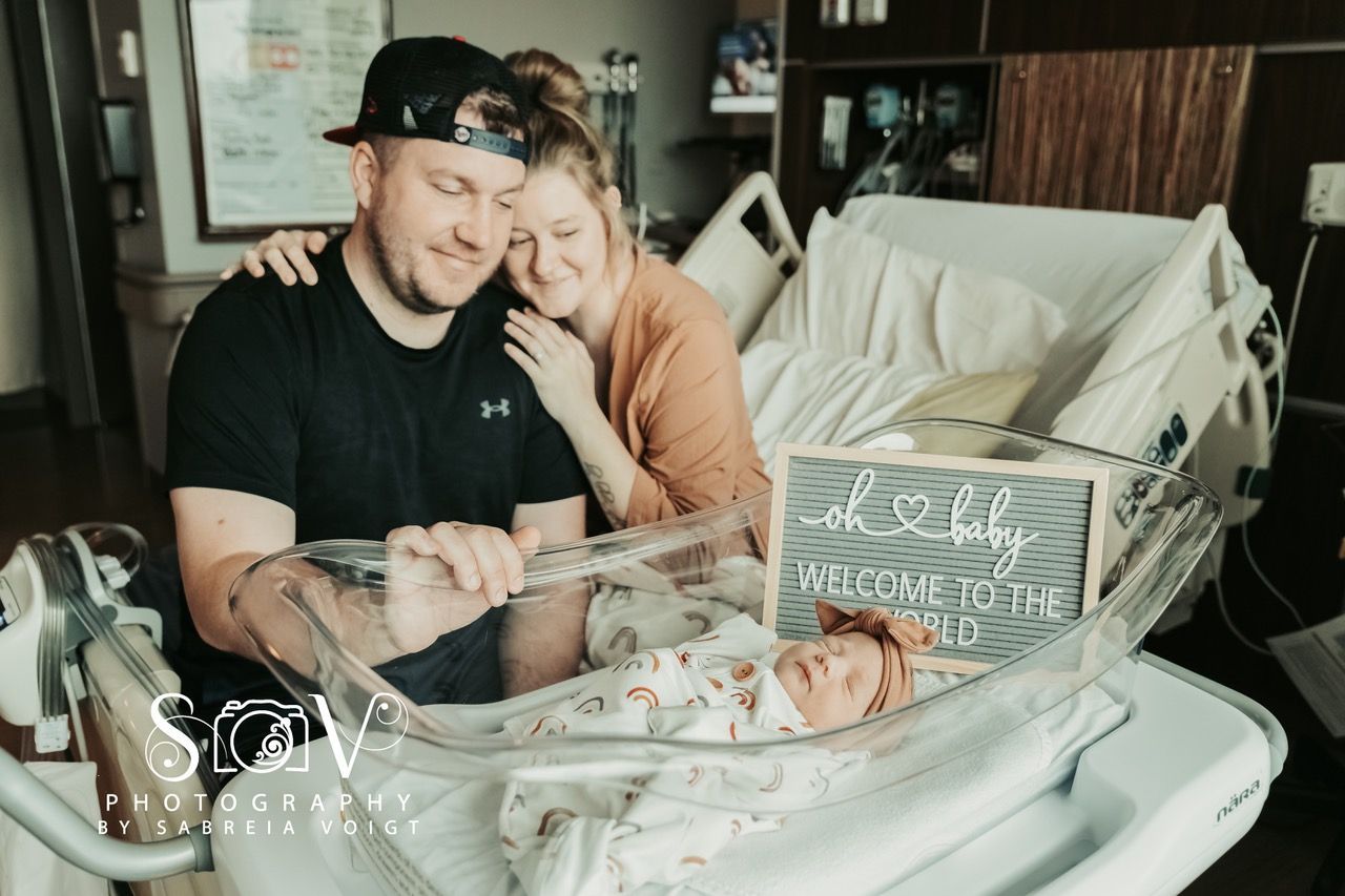 Parents gaze at newborn in hospital bassinet, welcoming baby to the world.