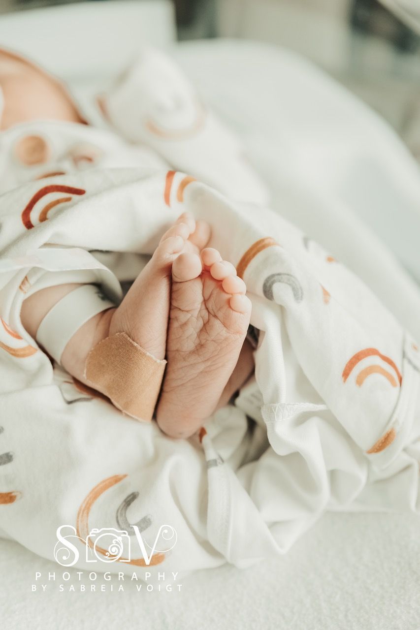 Close-up of newborn's feet, wrapped in a blanket with rainbow pattern, hospital setting.