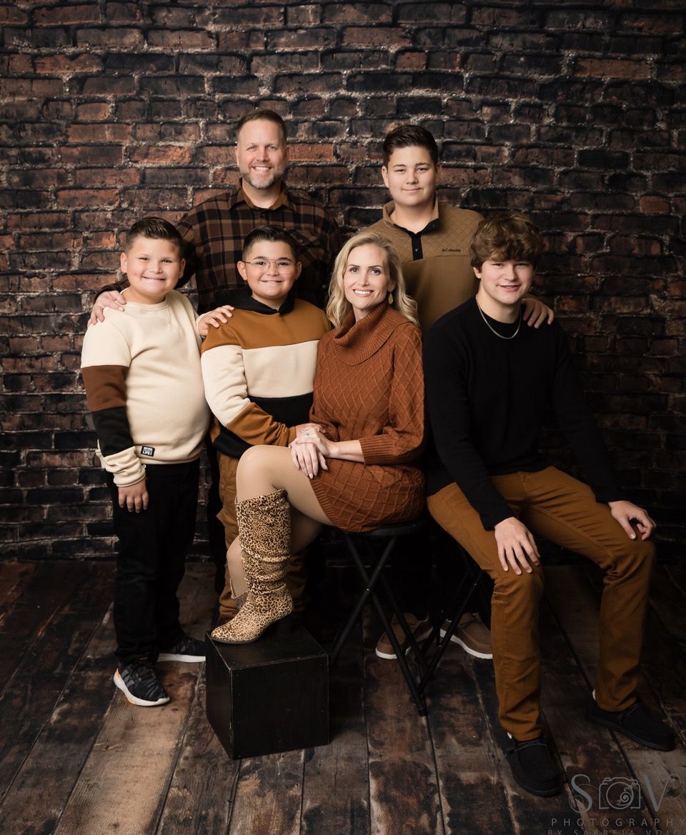 Family portrait against a brick wall. Six people smiling, posing in casual outfits.