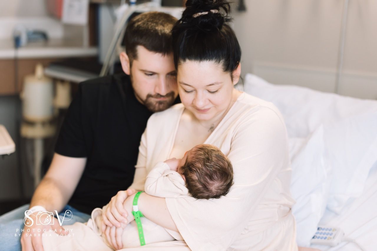 Parents gaze lovingly at newborn baby wrapped in blanket. Hospital room setting.