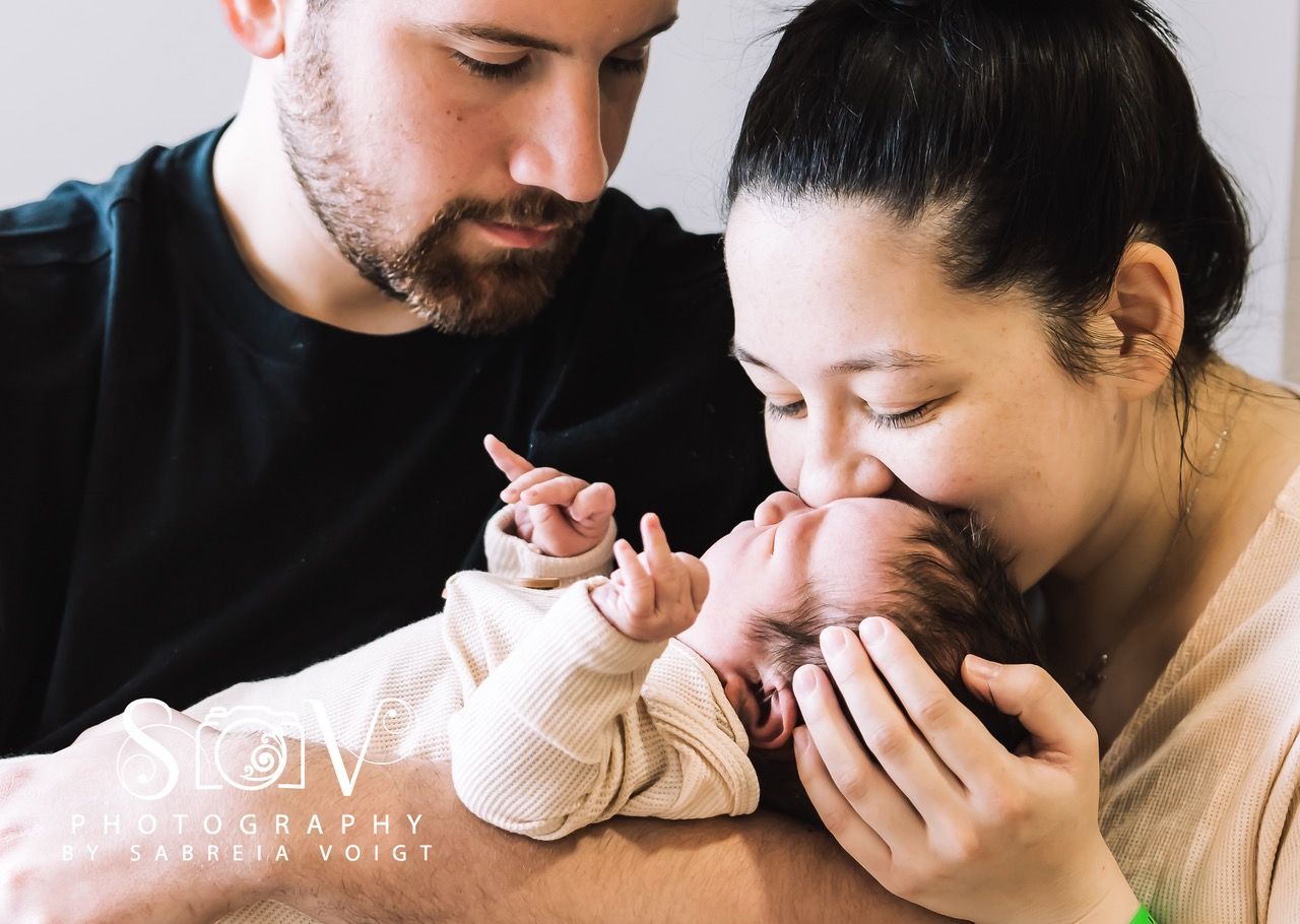 Parents kissing a newborn baby, indoor setting.