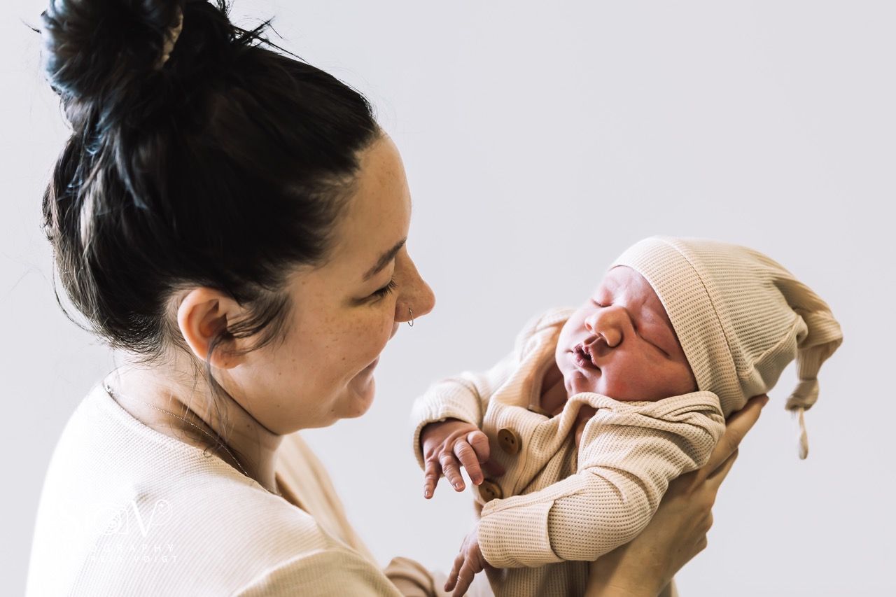 Woman holding a sleeping infant wearing a cream-colored knit cap and outfit.