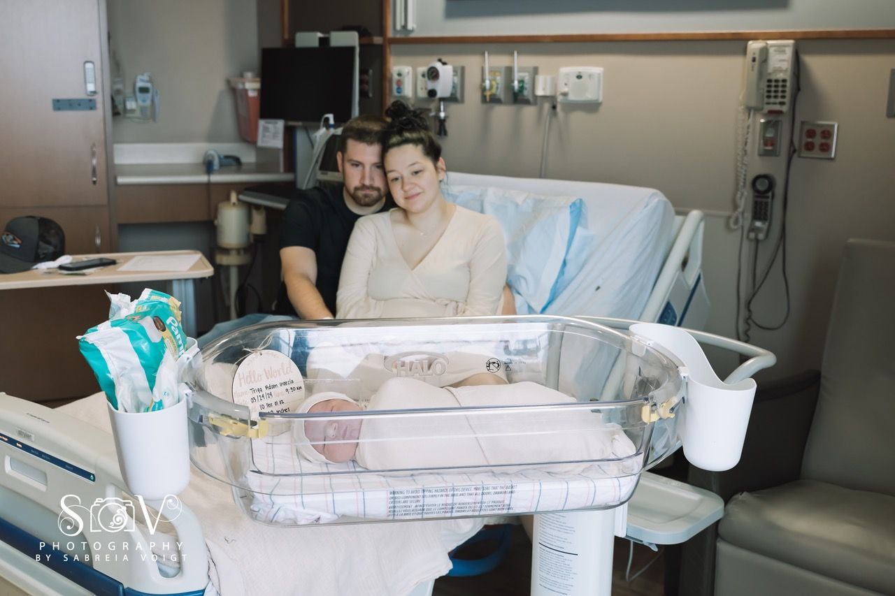 New parents in hospital room, gazing at their newborn baby in a bassinet.