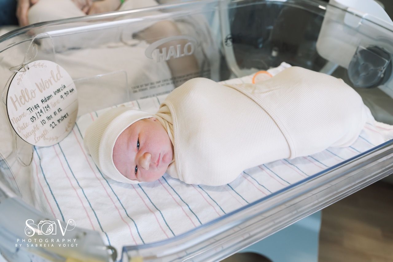 Newborn baby swaddled in a hospital bassinet, wearing a hat, with a 