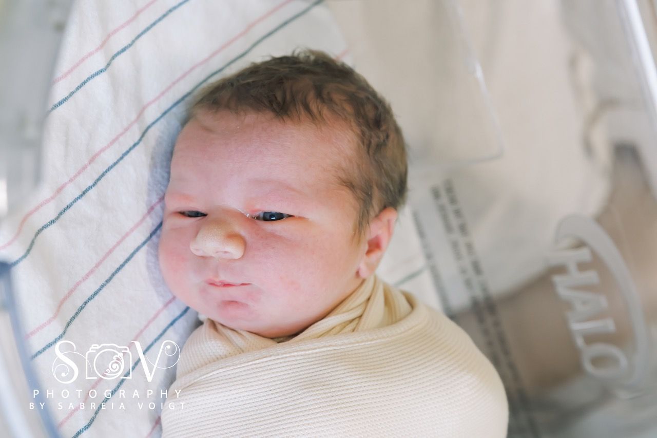 Newborn baby swaddled in a hospital bed, looking at the camera.