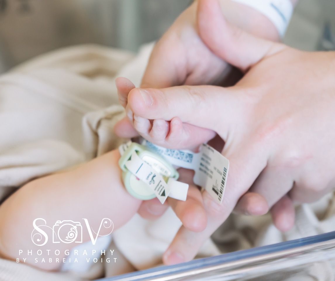 Adult hand holding a newborn's tiny hand with hospital wristband; soft lighting.