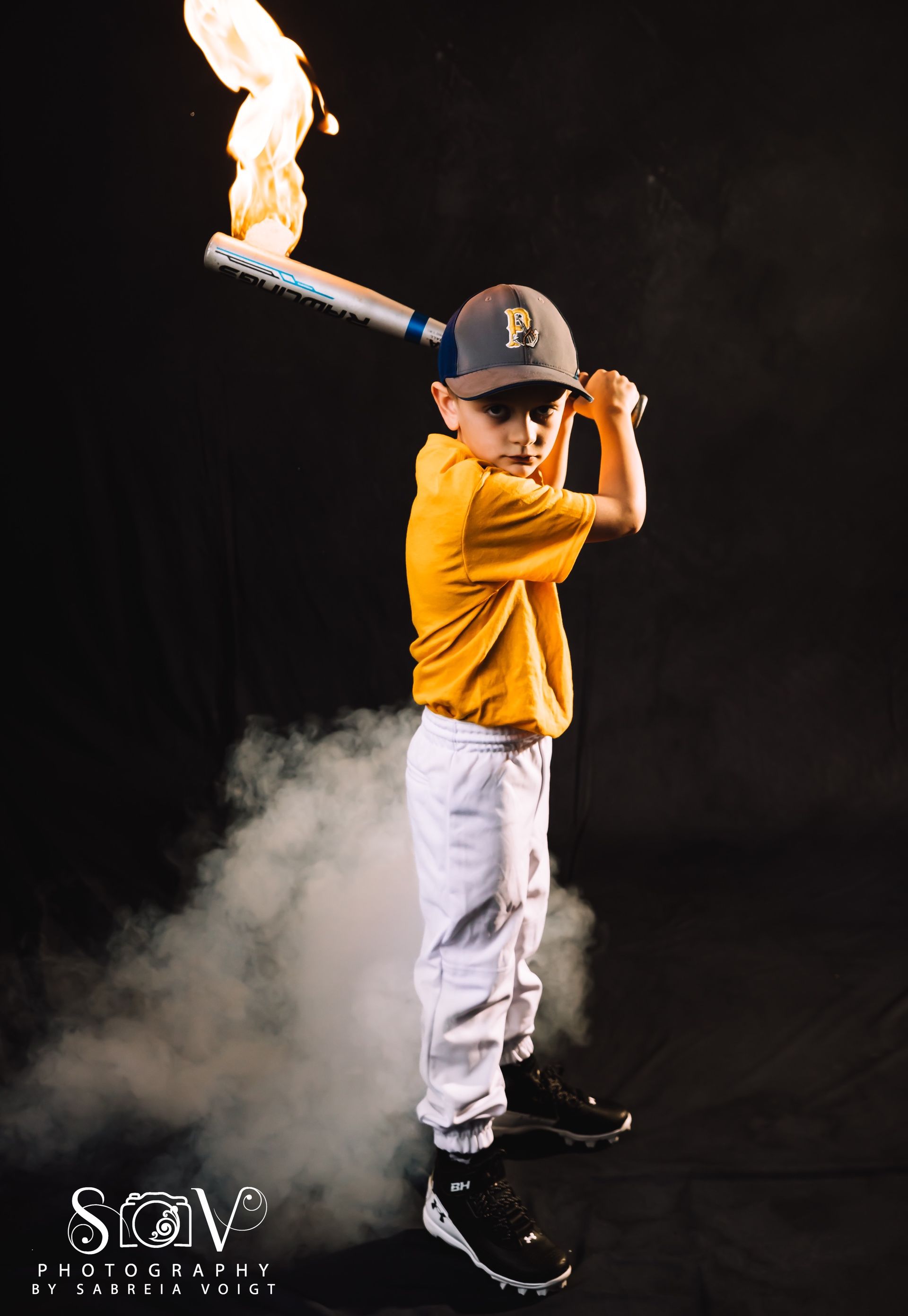 Boy in baseball uniform holding bat engulfed in flames, dark background with smoke.