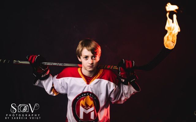 Hockey player holding a flaming stick. Red and white jersey against a dark background, looking forward.