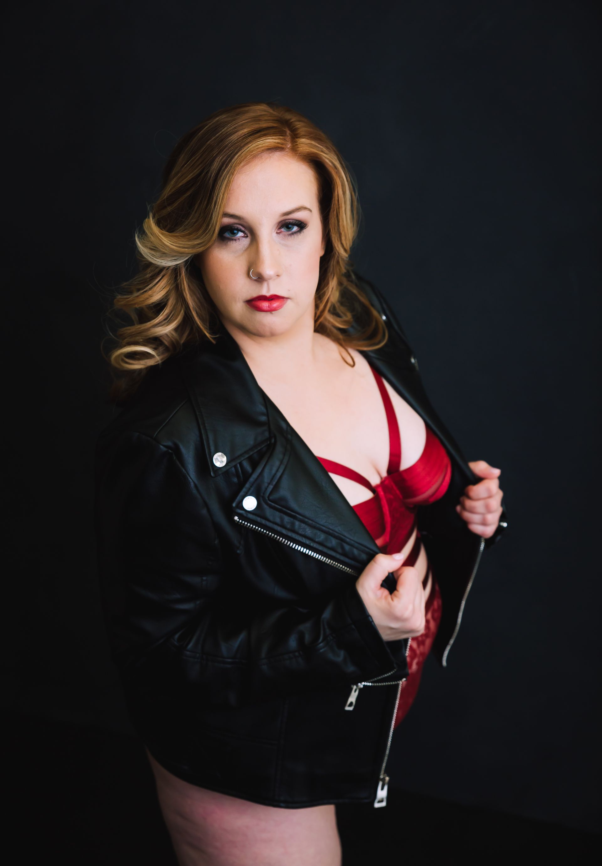 Woman in red lingerie, black leather jacket, opening jacket, dark background.