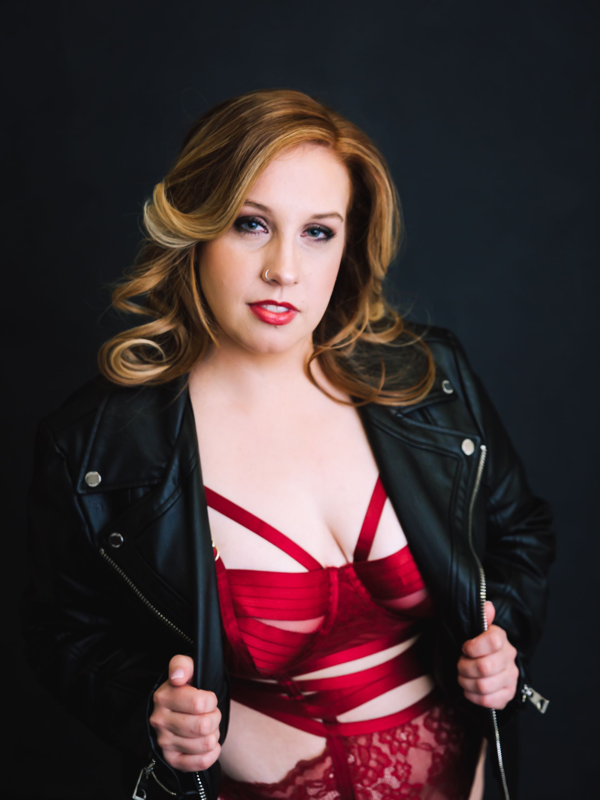 Woman in red lingerie and black leather jacket, looking at camera. Dark background.