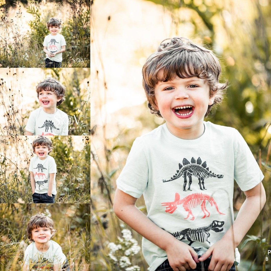 Boy with a dinosaur shirt laughing in a sunny field.
