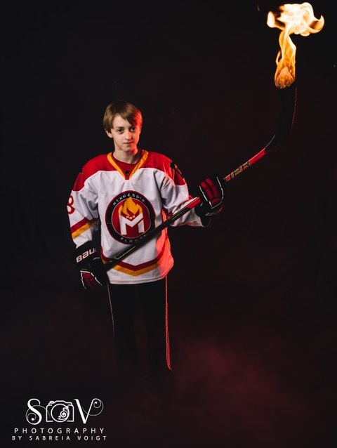 Hockey player in team jersey holds flaming hockey stick against a dark backdrop.