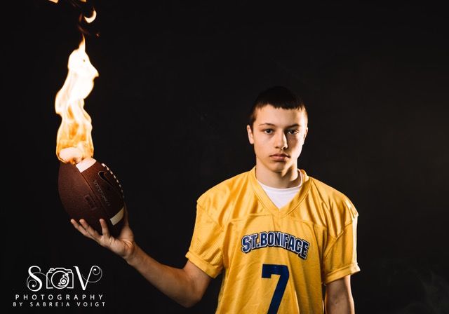 Football player holding flaming football, wearing yellow jersey against black backdrop.