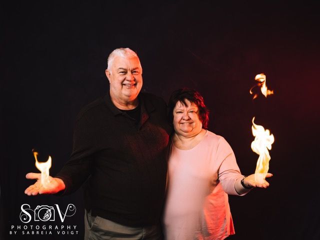 Couple holding flames, smiling in front of a dark backdrop with red lighting.
