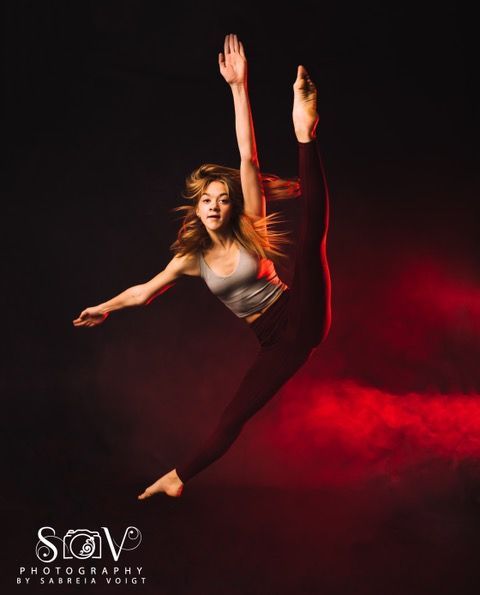Dancer in a dynamic leap, split leg extended. Arms outstretched. Red and black background.