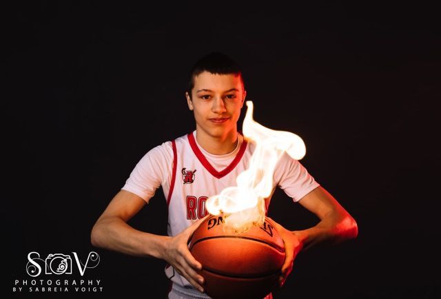 Basketball player holding flaming ball against a black background, lit with red and orange.