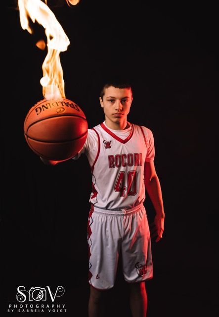 Basketball player holding flaming ball, wearing red and white jersey, standing against a black background.