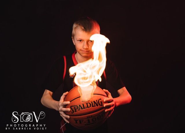 Boy holding a basketball on fire against a black background.