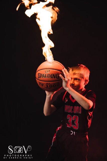 Boy in basketball jersey holding flaming basketball against black background.