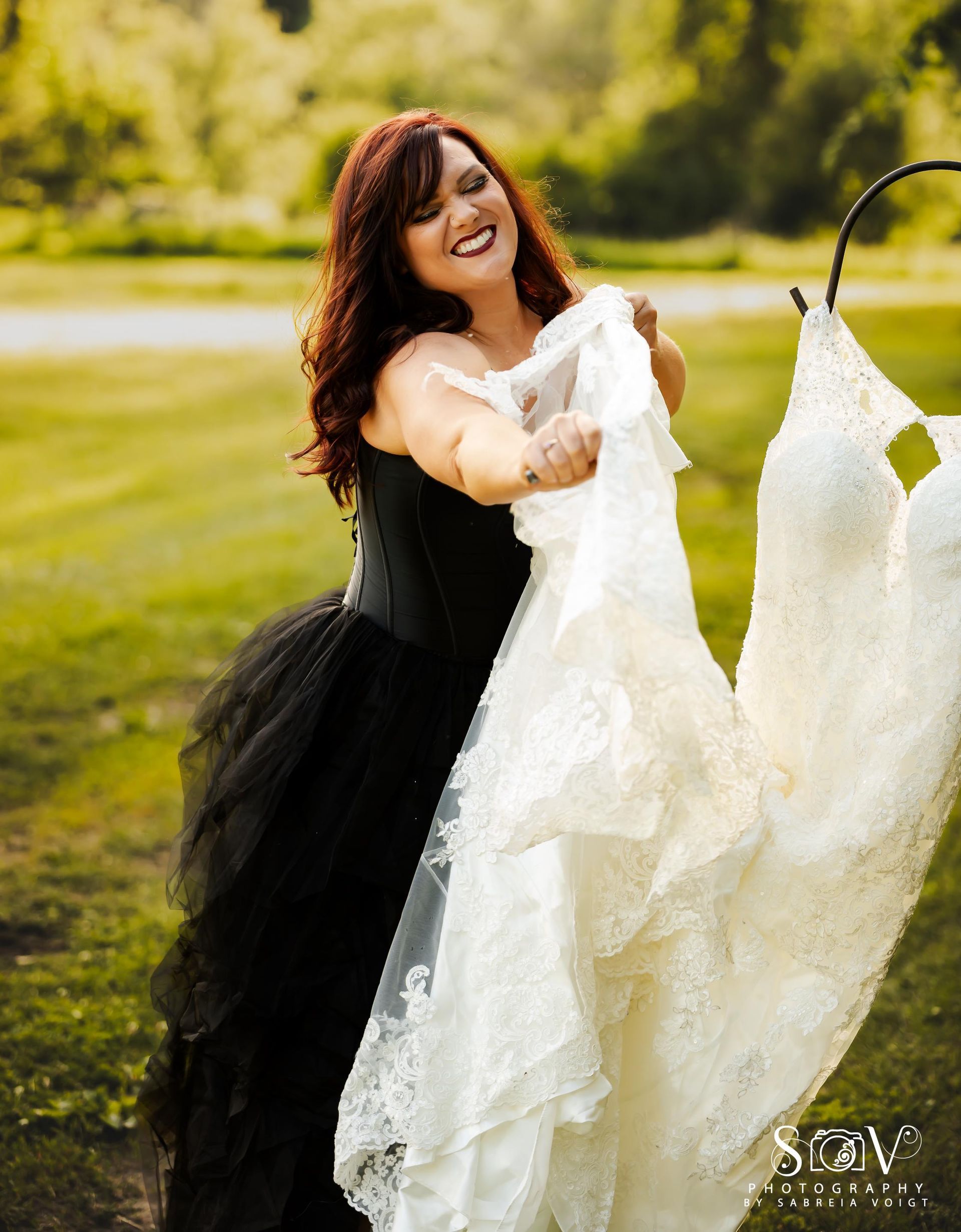 Woman holding a white wedding dress and smiling while wearing a black dress outside.