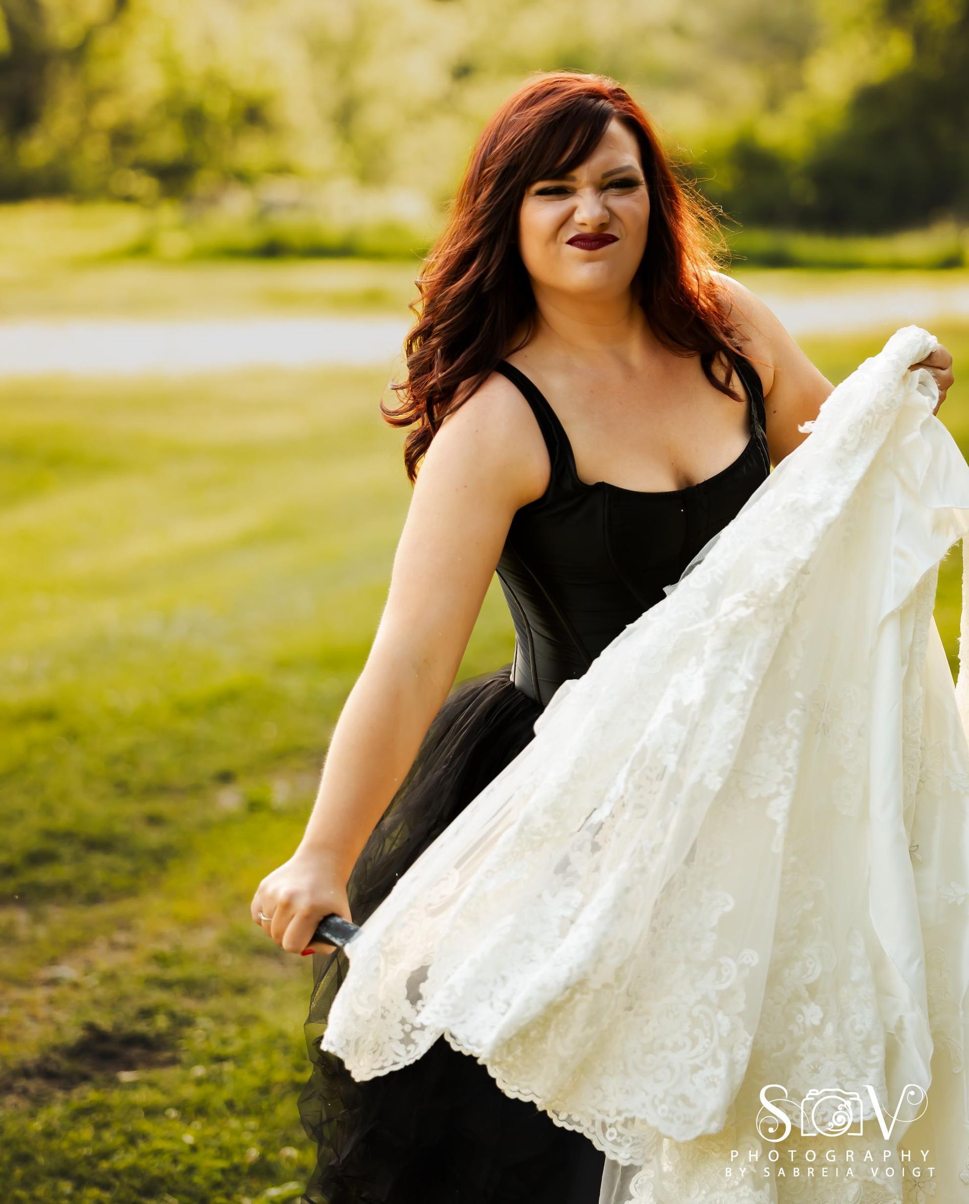 Woman in black dress, holding white wedding dress outdoors, making a face.