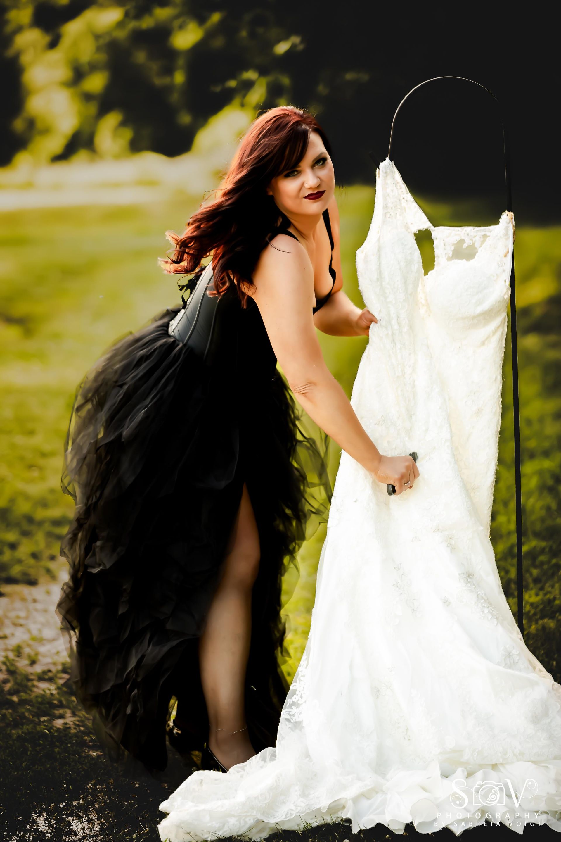 Woman in black dress touches white wedding dress outdoors.