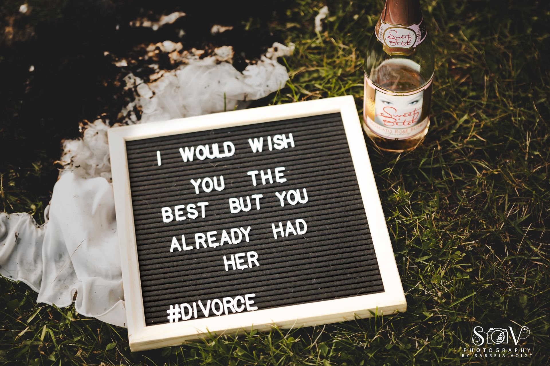 Black letter board with message about divorce, near a bottle and white fabric, on grass.