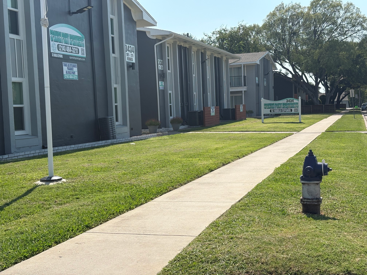 Apartment complex with a sidewalk and grassy lawn. A blue fire hydrant sits in the grass.