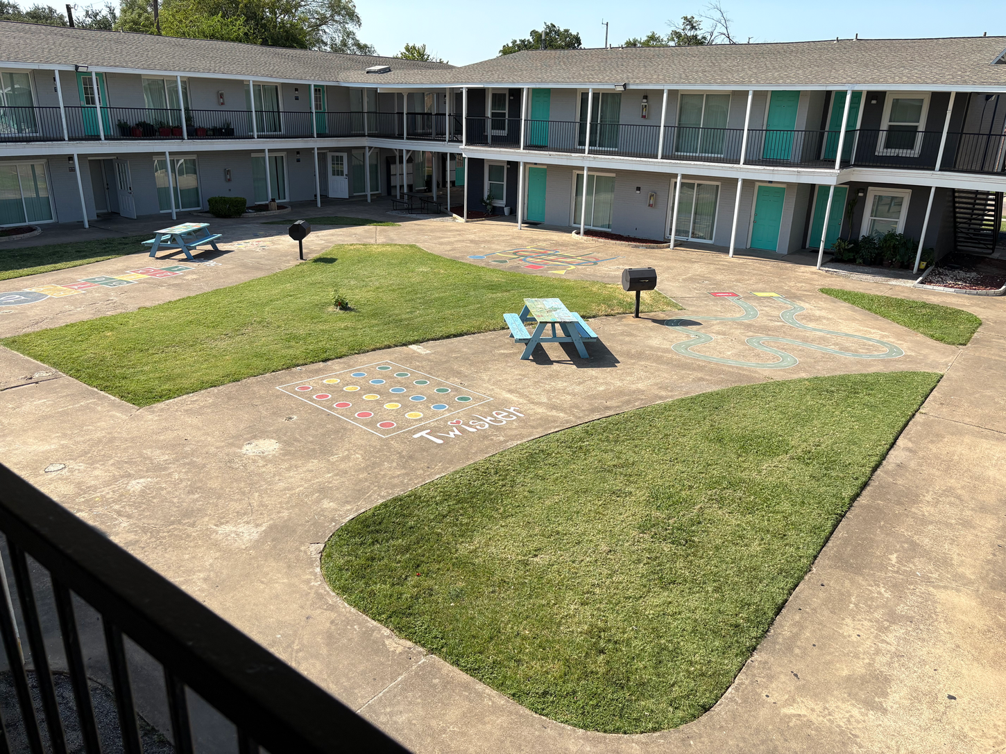 Courtyard apartment complex with green grass patches, picnic tables, and turquoise doors.