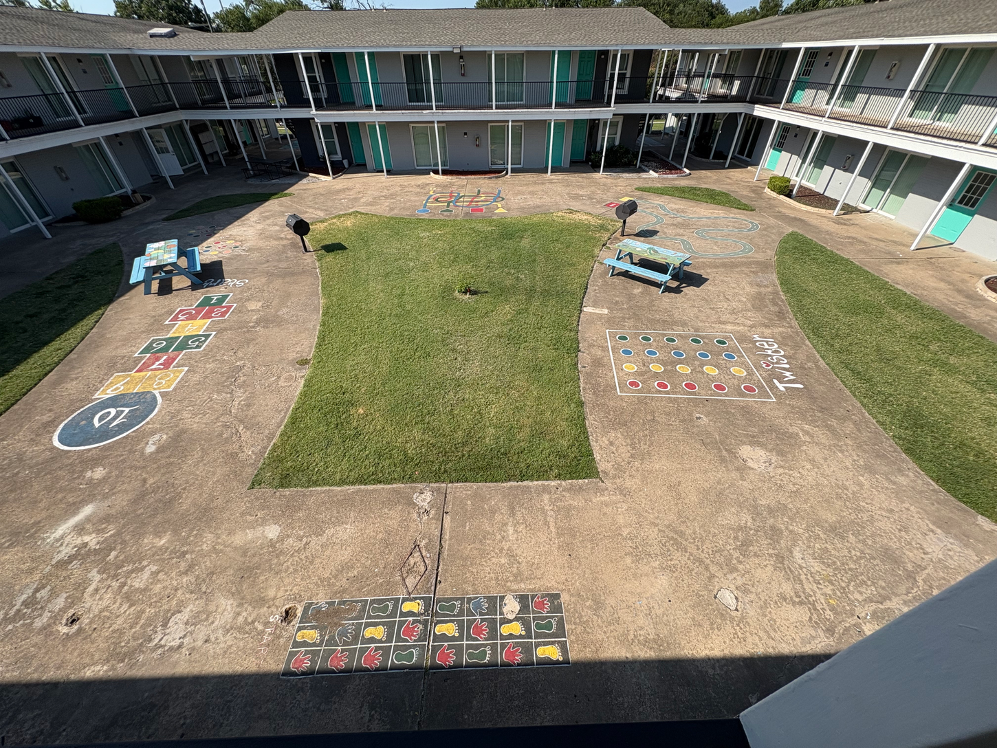 Courtyard with painted games on concrete, grass patch, two-story building with turquoise accents.