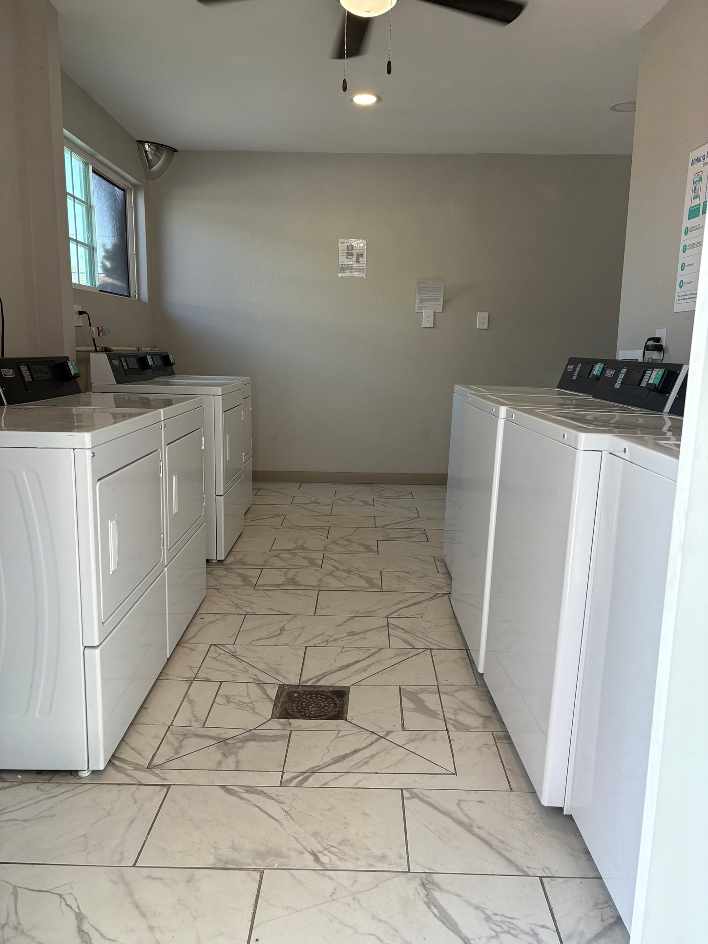 Laundry room with white washers and dryers on marble-patterned floor.