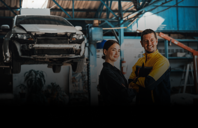 Two auto mechanics in a garage with a car on a lift. Both are smiling, with arms crossed. | Strong's Alignment Service
