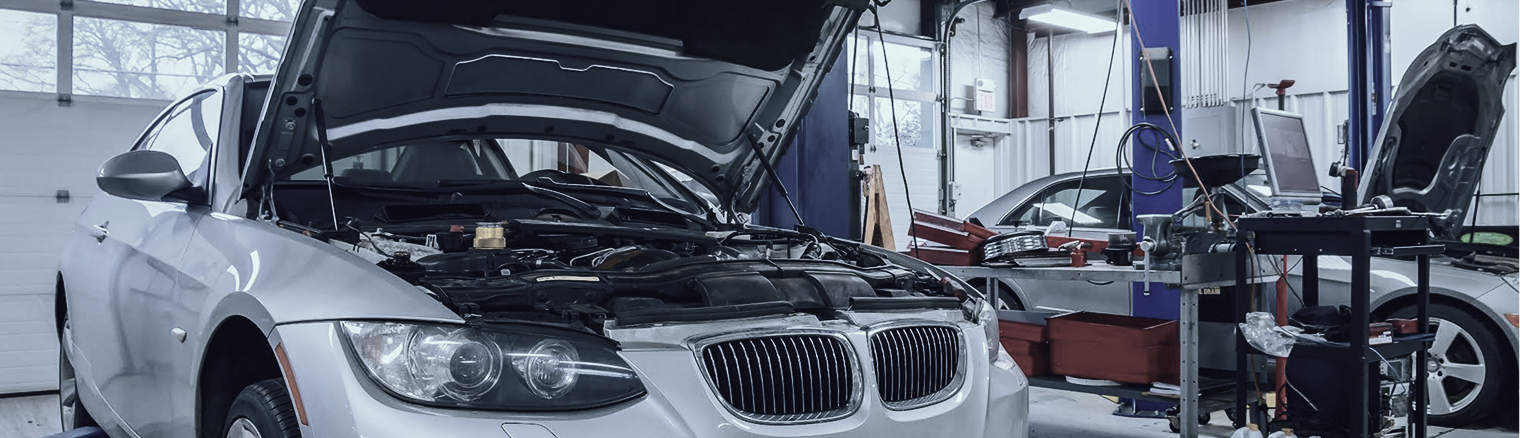 A silver car with its hood open in an auto repair shop. Another car and a mechanic are visible. | Strong's Alignment Service
