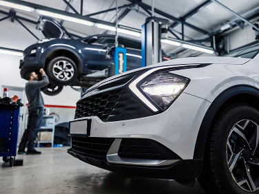 Car in auto repair shop with mechanic working on a raised vehicle. Another car in foreground. | Strong's Alignment Service