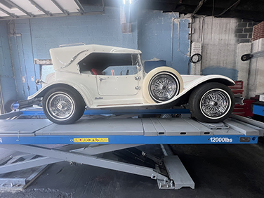 White vintage car on a lift in a garage. | Strong's Alignment Service