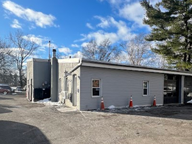 Gray commercial building with snow on the ground, orange traffic cones, and a cloudy blue sky. | Strong's Alignment Service