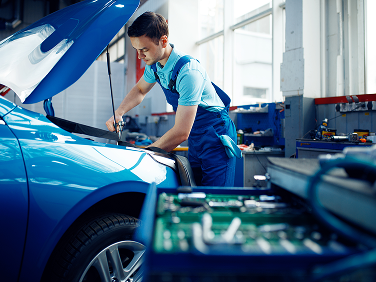 Mechanic working on a blue car engine in a garage with tools. | Strong's Alignment Service