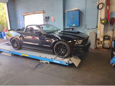 Black Ford Mustang convertible on a lift in a repair shop. | Strong's Alignment Service