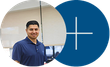 Man in a navy polo standing beside a blue circle with a white plus sign in an office setting