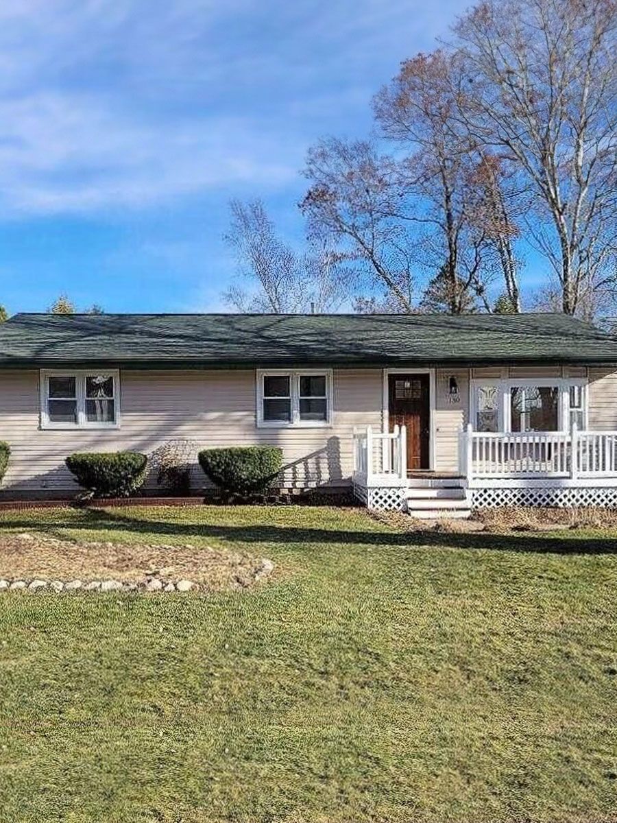 A white house with a green roof and a large lawn in front of it.