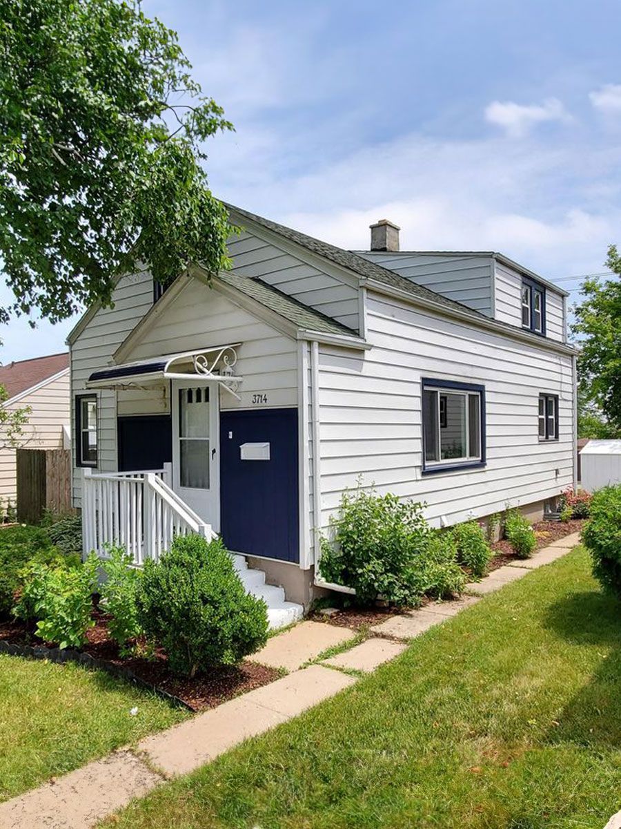 A white house with a blue door and stairs is sitting on top of a lush green lawn.