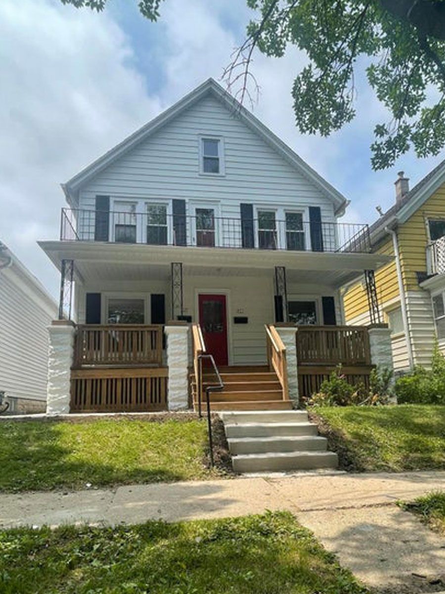 A white house with a red door and stairs in front of it.