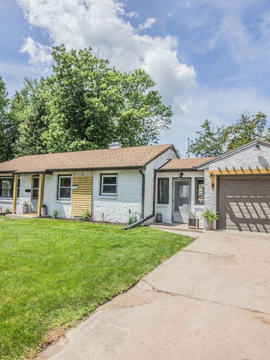 A white house with a brown roof and a garage is for sale.