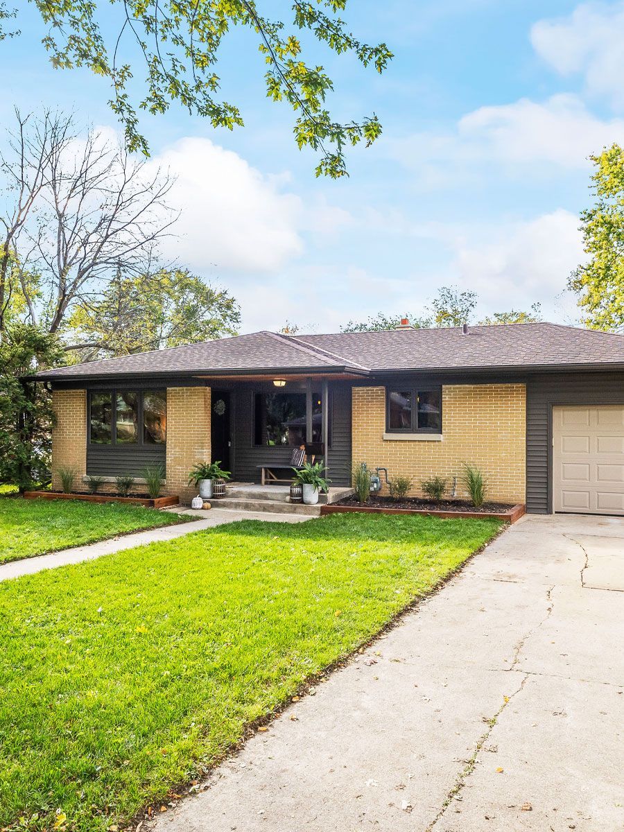 A brick house with a lush green lawn and a driveway leading to it.