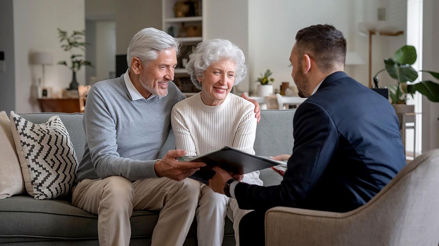 An elderly couple is sitting on a couch talking to a man in a suit.