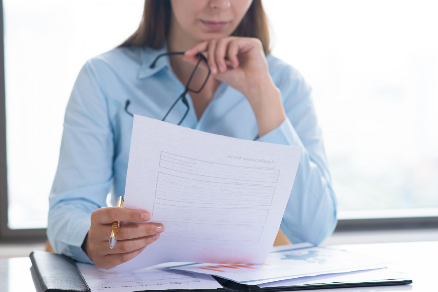 A woman is sitting at a desk holding a piece of paper.