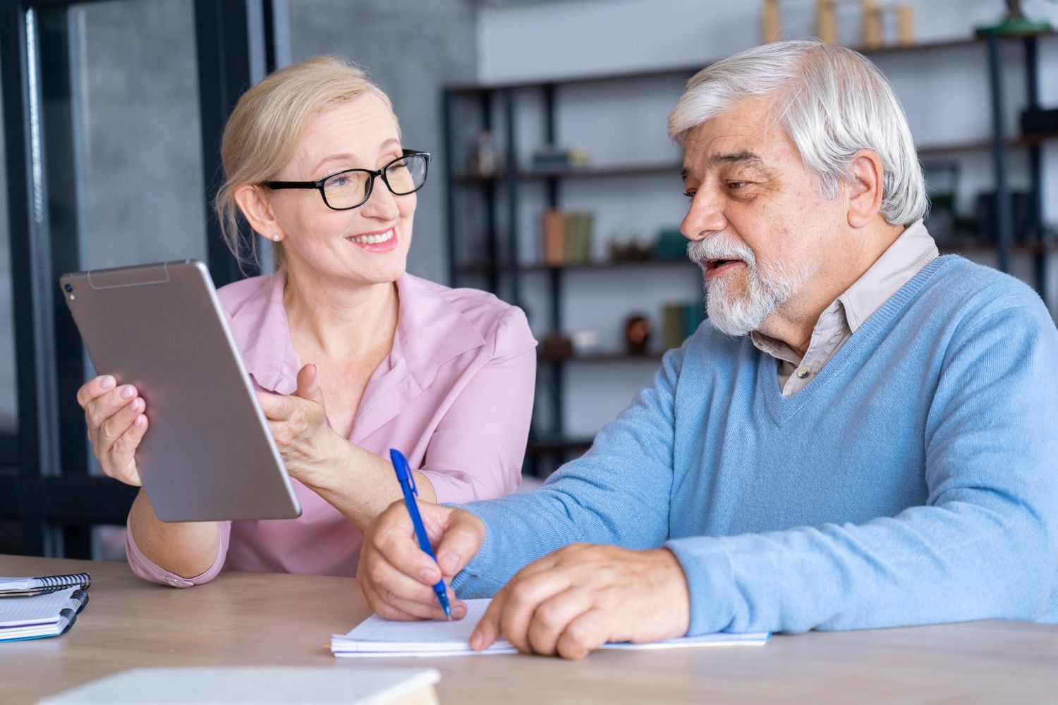 A man and a woman are sitting at a table looking at a tablet.