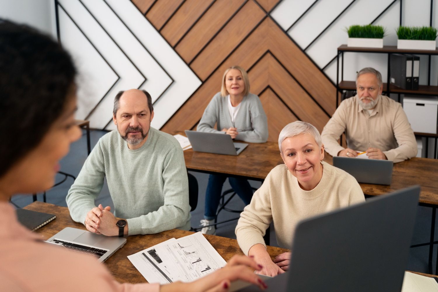 A group of older people are sitting at a table with laptops.